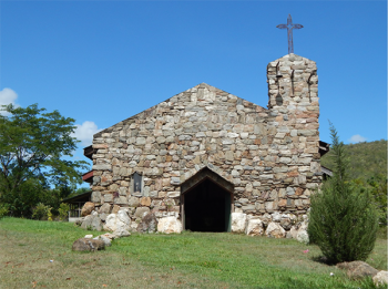 A photo of an old stone church with green grass in the foreground and a blue sky in the background.