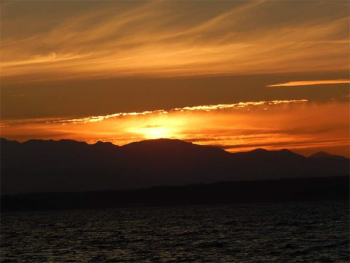 A photo of a golden sunset with mountains and water visible in the foreground.
