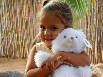 Photo of a young girl smiling and hugging a stuffed animal.