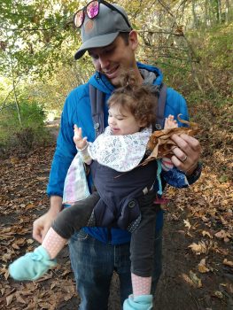 A man in a wooded park holding a baby.