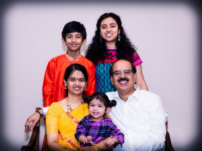 A smiling family of two parents and three children posing for the camera with a white background.