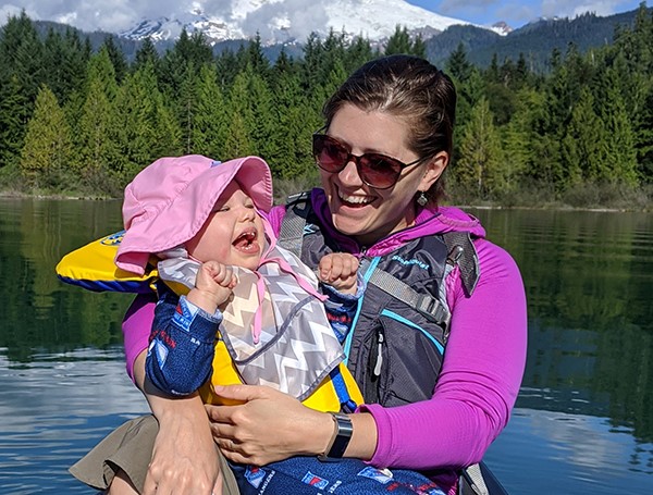 A woman holding a toddler with a lake and a forest in the background