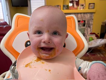 Photo of a baby smiling with food on his bib.