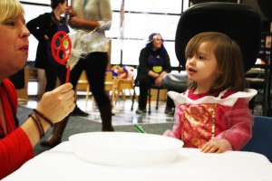 A Spirit of Children volunteer blows bubbles for a little girl in the playroom who is dressed as a Disney princess.