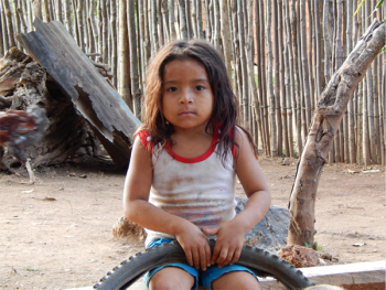 Photo of a young girl with hair to her shoulders wearing a white t-shirt and holding a bicycle tire. A wooden fence in the background.