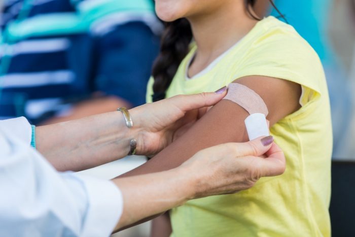 Child getting a band aid on flu shot site on right arm